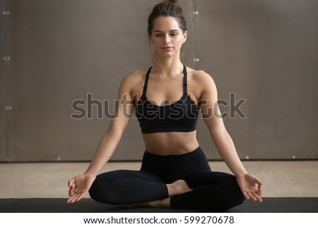 Young attractive happy yogi woman practicing yoga, sitting in Sukhasana exercise, Easy Seat pose with mudra, working out wearing black sportswear, cool urban style, full length, grey studio background Royalty-Free Stock Photo #599270678
