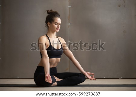 Young attractive sporty yogi woman practicing yoga, sitting in Sukhasana exercise, Easy Seat pose, working out wearing black sportswear, cool urban style grey studio copy space background, full length Royalty-Free Stock Photo #599270687