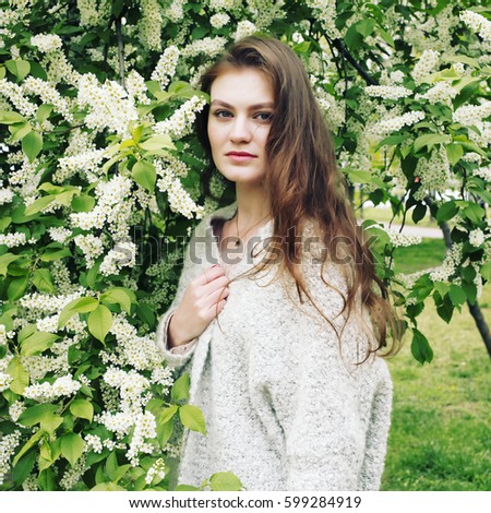 Beautiful blonde young woman wearing fashionable clothes, gray knitted cardigan posing in the garden with blooming trees. Fashion photo, springtime, face care, clean skin