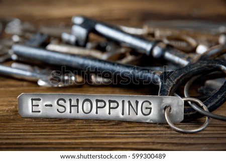 Photo of key bunch on wooden board and tag with letters imprinted on clean metal surface; concept of E-SHOPPING