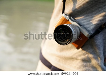 Photographer with mirrorless camera. Standing outdoors with the camera hanging on the shoulder Royalty-Free Stock Photo #599314904