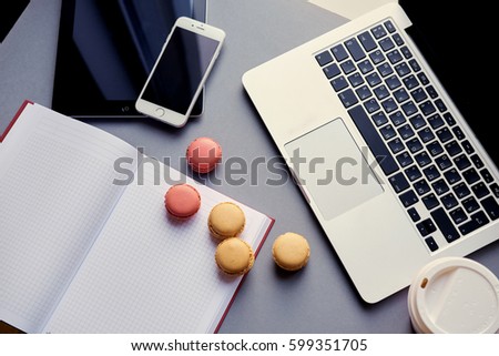 Open laptop, smart phone and tablet PC and small cakes on a table.