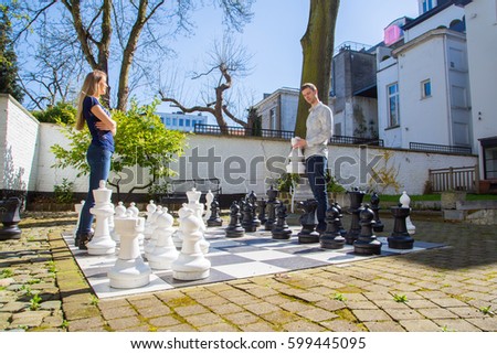 Young man and woman playing outside large chess in the yard. Looks like the girl is winning. Great outside activity.