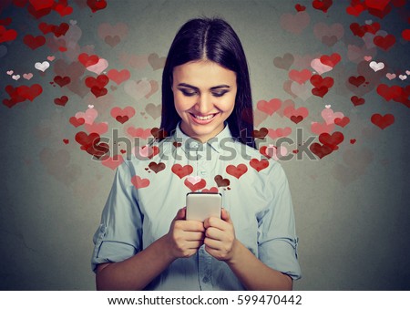 Beautiful happy woman sending love text message on mobile phone with red hearts flying away from screen isolated on gray background. Positive human emotions face expressions  Royalty-Free Stock Photo #599470442