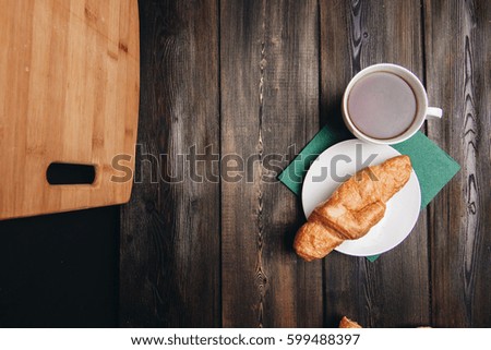 Croissants on a saucer, coffee in a mug, on a green napkin, cutting board