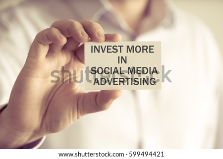 Closeup on businessman holding a card with text INVEST MORE IN SOCIAL MEDIA ADVERTISING, business concept image with soft focus background and vintage tone