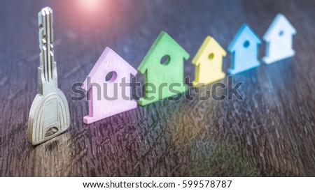 Silver Key staying in Line with Miniature Symbol of Various Coloured Houses on dark wooden surface