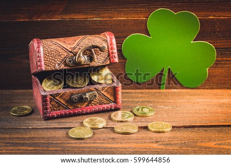 A chest with gold coins on a wooden background. Clover leaves. St.Patrick 's Day