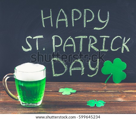 The inscription with green chalk on a chalkboard: Happy St. Patrick's Day. Clover leaves. A mug with green beer