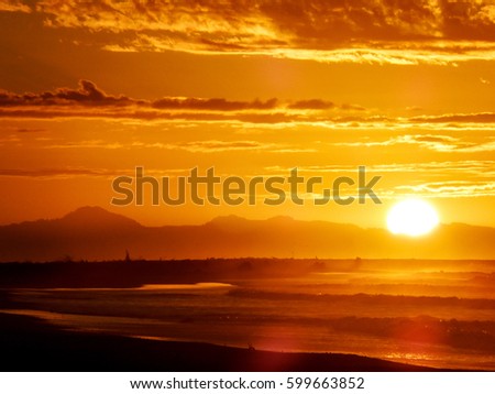 Beautiful golden sunset over the Pacific ocean, taken from Haast Beach in the south of New Zealand. Showing waves and silhouetted mountains and bush.