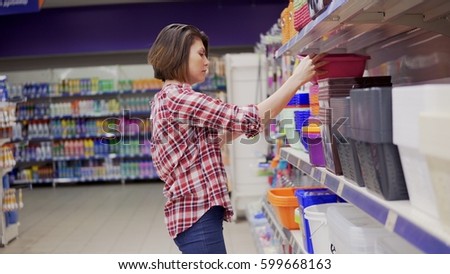 A young woman in check shirt is choosing plastic box in the shopping center. 4k