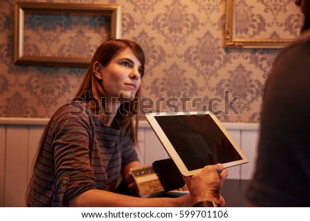 Young waiter types something on his tablet with credit card while a young woman is looking at him with interest