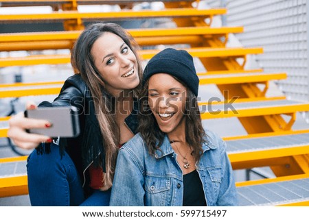 Two young and beautiful women take a selfie on yellow iron staircase in the city