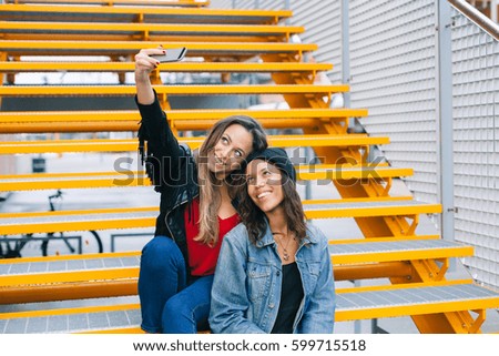 Two young and beautiful women take a selfie on yellow iron staircase in the city
