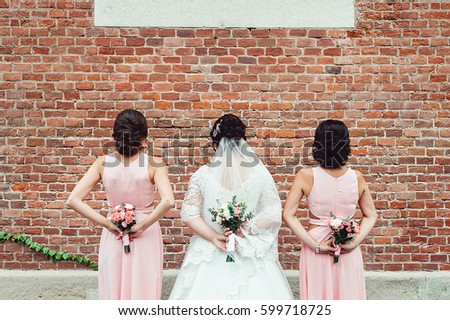 Bride and bridesmaid standing face to orange brick wall and holding in a back wedding bouquets