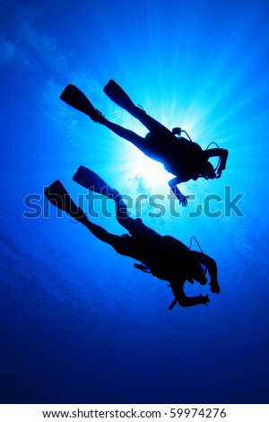 Couple scuba diving, silhouetted against sun