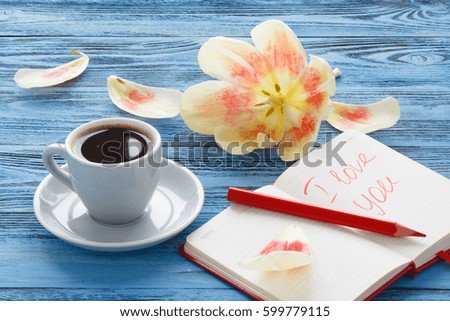 Cup of coffee and litter notebook with word "i love you" on the table and flower