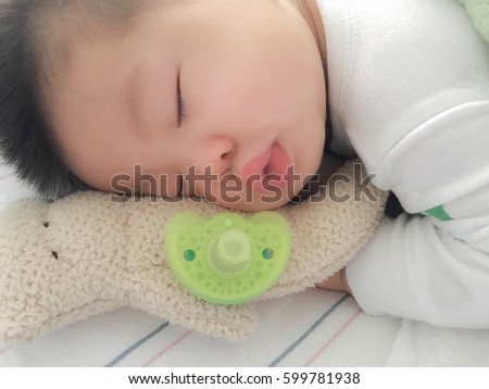 Soft focus on baby's cute little face, stuffed doll and plastic baby soother pacifier. Concept of childcare, joy, hope, love, pacify, bonding and care...