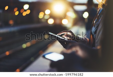 Enjoying travel. Young woman waiting on station platform on background light electric moving train using smart phone in night. Tourist text message and plan route of stop railway, railroad transport Royalty-Free Stock Photo #599796182