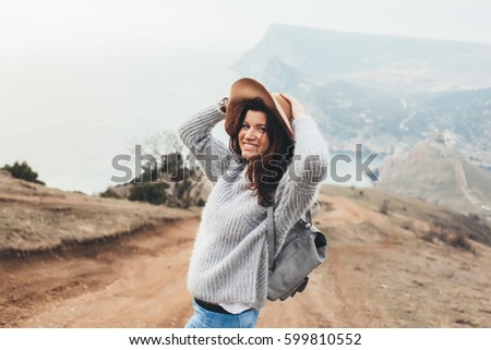 Girl wearing hat and sweater travel in mountains alone. Cold weather, calm scene. Backpacker walking outdoors in fall, back view over landscape. Wanderlust photo series.