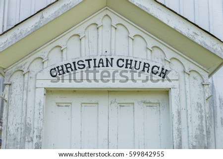 Close up of Christian Church sign above the doors to a white painted church.