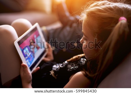 Little girl in black dress watching cartoon sitting on couch in bright living room