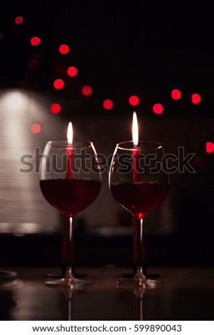 Two glasses of wine and candels are in the dark with new year lights at the background