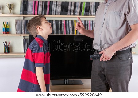 Strict dad holding the remote control not allowing watching the TV for his son  Royalty-Free Stock Photo #599920649