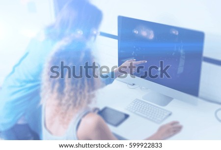 Two young girl working on desktop computer in modern coworking studio.Coworkers using electronics gadgets.Icons,graphs and diagramm on monitor.Visual effect,color filter, blurred.Horizontal