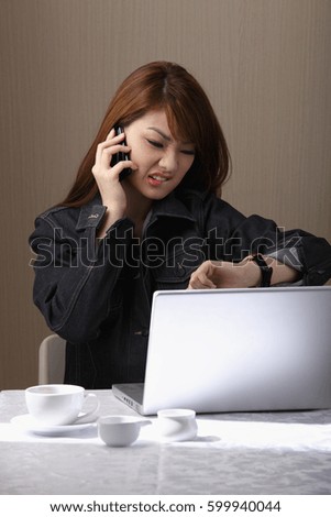 Young woman talking on phone, looking at watch and making a face.