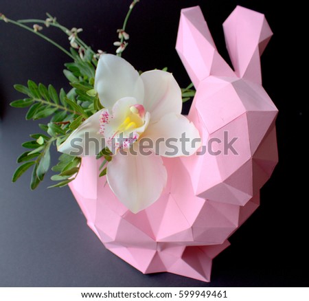 Pink paper rabbit with orchid flower on black background.Easter bunny with flower