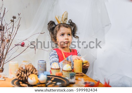 little girl 2 - 4 years in a red dress draws intently the pictures on the eggs with watercolors . at the head of the child ears of a rabbit preparing for Easter