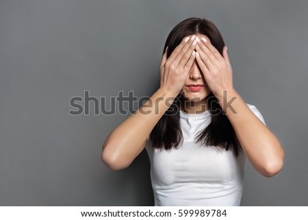 See no evil concept. Portrait of young scared woman covering eyes with hands while standing against gray studio background. Confused girl close eyes with palms ignoring something Royalty-Free Stock Photo #599989784