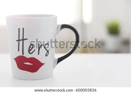 coffee mug on a white table in the morning, with hers graphic, and blurred background  Royalty-Free Stock Photo #600003836