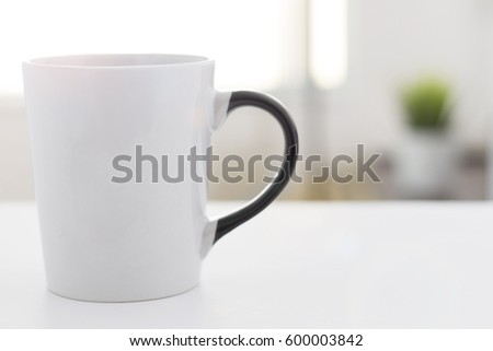 white coffee mug with black handle, on a withe table and blurred background in the morning Royalty-Free Stock Photo #600003842