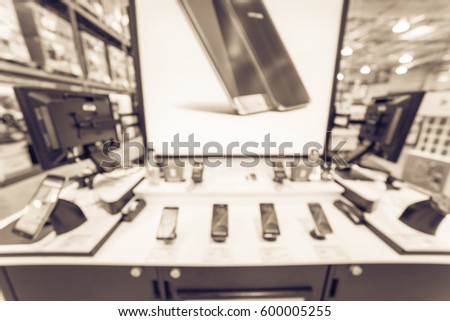 Blurred variety of modern smart phones on display at cellphone department in distribution warehouse or storehouse. Defocused background of technology inventory, hypermarket, wholesale bokeh light.