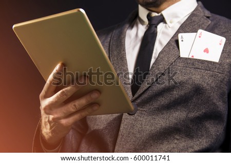 Closeup of man, face not showing, holding tablet and two aces in pocket / poker concept 
