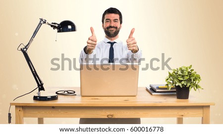 Businessman in his office with thumb up on ocher background