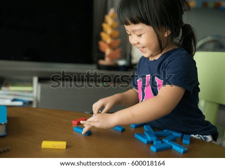 Little girl playing with wooden blocks the unstable tower.Building collapse games.Children imagination or creativity concept.Little asian girl playing with colorful toy blocks. 