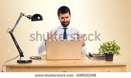 Businessman in his office making horn gesture on ocher background