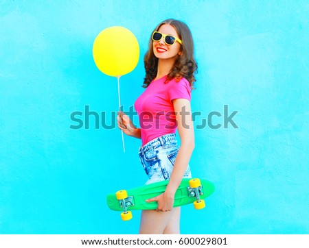 Fashion pretty woman with yellow air balloon and skateboard having fun over colorful blue background