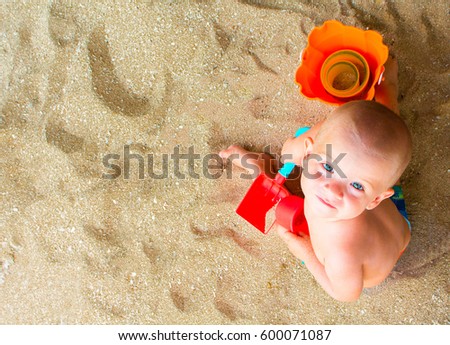Child plays with sand on beach. Cute baby boy on white beach. Tropical seaside vacation with baby. Blue eyes boy on summer holiday. Child with red scoop and bucket photo. Childhood on seaside banner