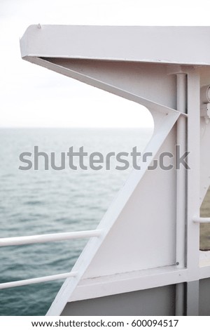 Abstract angle and line art of white painted reinforced metal wall and steel railing of nautical ship vessel above pale blue horizon of open ocean waters under bright cloudy day in dreamy travel scene