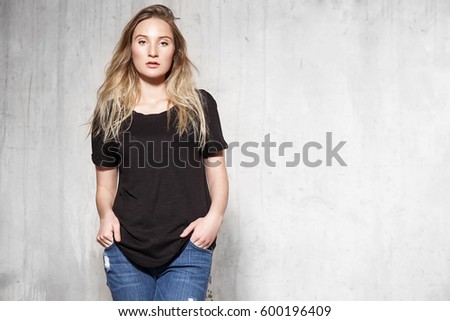 Beautiful blonde girl wearing a blank black t-shirt standing on a concrete wall background