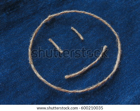 Emoji. Smiling emoticon made of twine on a blue denim background. Close-up