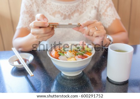 Blurred photo of young woman is taking the photo of Japanese sashimi dish by her smart mobile phone in Japanese restaurant. 