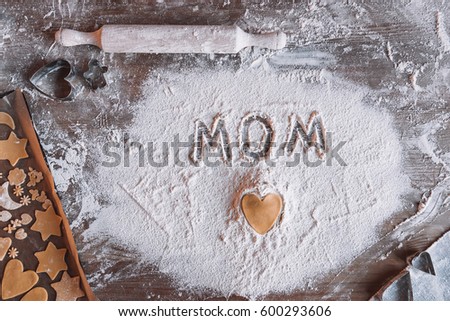 'Top view of uncooked heart shaped cookie and word mom written in flour, Mothers day concept