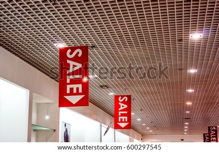 few red vertical sale posters with white letters hang from grid ceiling in big shop in sale season. sale poster board at fashion clothes shopfront