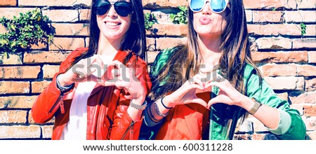 Cheerful young girlfriends having fun making heart shape next to old city wall - Happy smiling teen women doing hearts with hands outdoors - Joyful  female friends love gesture - Concept of friendship