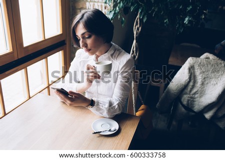 Spectacular young brunette, business woman drink coffee, using gadgets in cafe and looking to window
